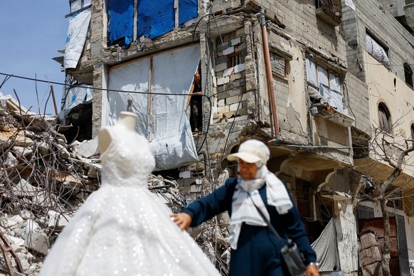 A Palestinian woman looks at a wedding dress displayed outside a shop next to debris and damaged buildings, as brides in Gaza turn to reused gowns amid soaring prices and shortages caused by the war,  ...