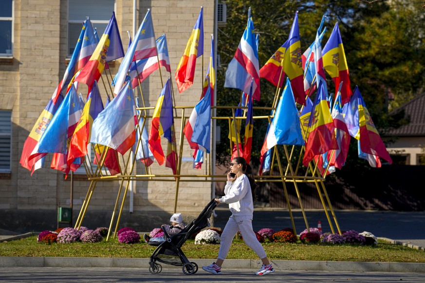 A woman pushes a baby stroller backdropped by moldovan and gagauz flags in Comrat, the capital of Gagauzia, an autonomous part of Moldova, Saturday, Nov. 2, 2024, ahead of a presidential election runo ...