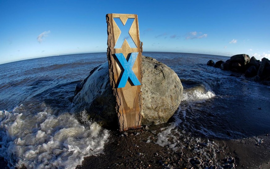 epa05075864 A plank of wood with a blue cross as a resistance mark is placed on the beach in Fehmarn, Germany, 19 December 2015. Opponents of the Fehmarnbelt link are not giving up and symbolize their ...