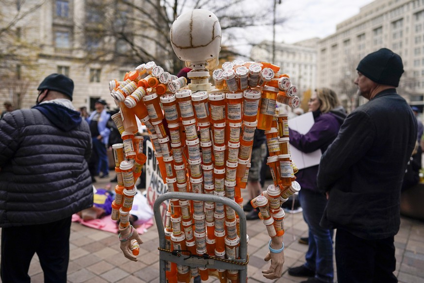 «Pill Mann» fabriqué par Frank Huntley, à droite, à partir de ses flacons de médicaments sur ordonnance contenant des opioïdes. La sculpture est exposée lors d'une manifestation des défenseurs des victimes devant le ministère de la Justice à Washington, DC.