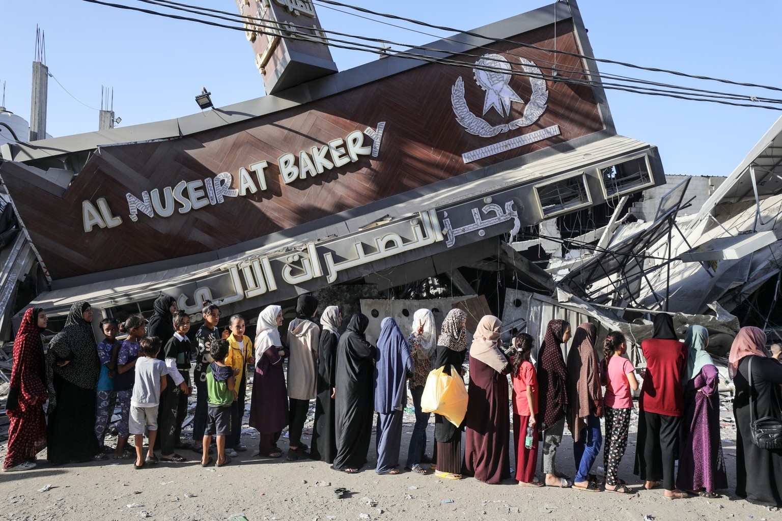 People queue for bread in front of a bakery that was partially destroyed in an Israeli strike, in the Nuseirat refugee camp in the central Gaza Strip, on November 4, 2023, as battles continue between  ...
