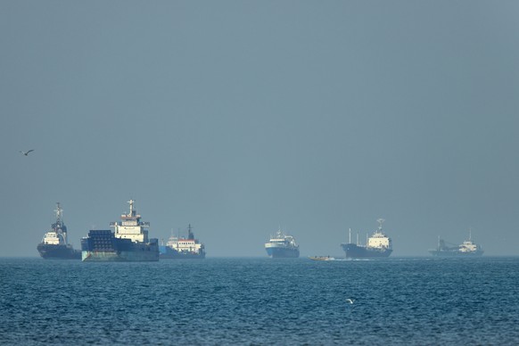 KEYPIX - Cargo ships, including bulk carriers and general cargo vessels, sit at anchor offshore as a small motorboat passes in the foreground, in the Strait of Hormuz off Bandar Abbas, Iran, Monday, M ...