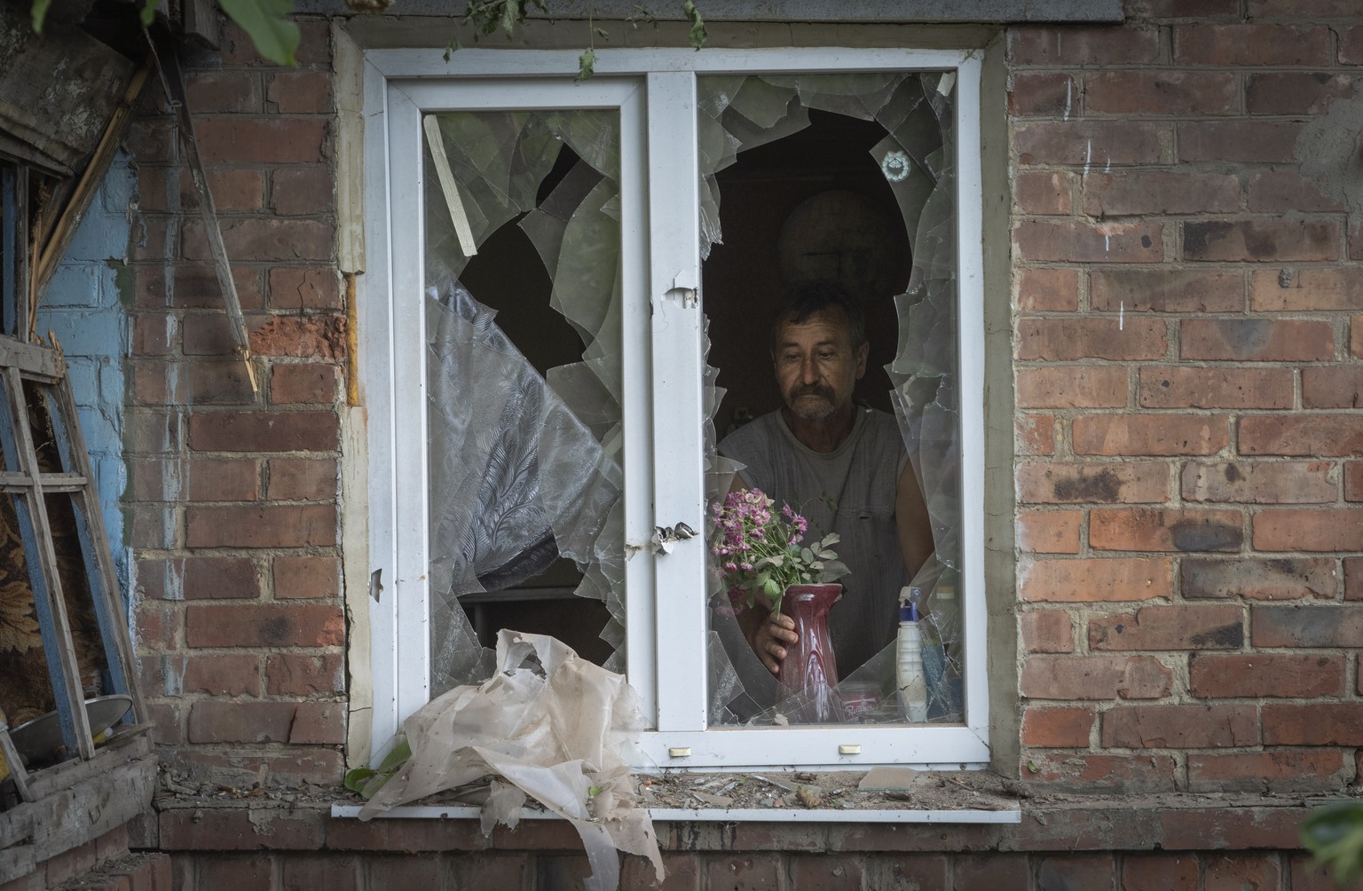 FILE - A local resident places a vase with flowers on a broken window in his house damaged by the Russian shelling in Bakhmut, Donetsk region, Ukraine, Sunday , June 26, 2022.(AP Photo/Efrem Lukatsky, ...