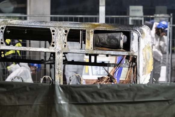Fire investigators examine the charred shell of a postal bus pictured after catching fire in Kerzers, Switzerland, Tuesday, March 10, 2026. According to the Fribourg cantonal police, several passenger ...