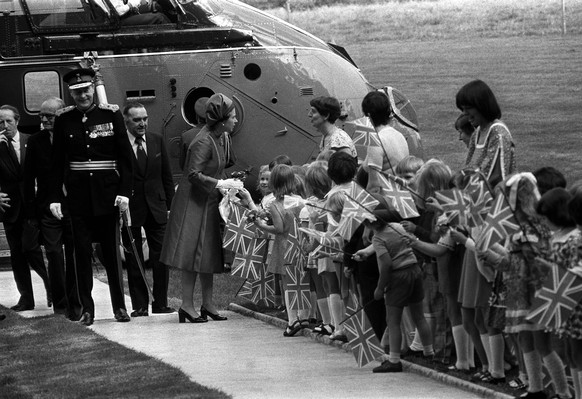Queen Elizabeth II with flag-waving children after her arrival by helicopter - her first ever flight in one - at historic Hillsborough Castle, 14 miles from Belfast, at the start of her 2 day Silver J ...