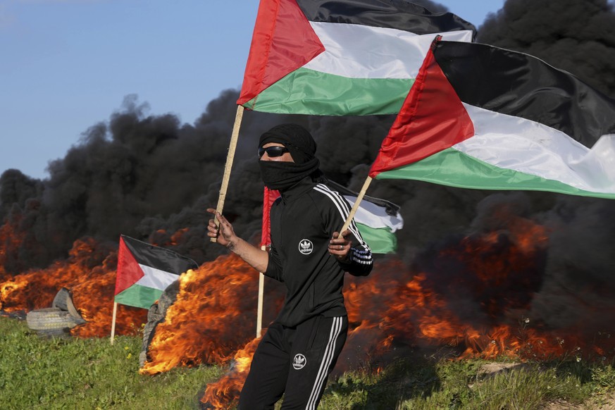 Un manifestant agite ses drapeaux nationaux tandis que d'autres brûlent des pneus lors d'une manifestation contre un raid militaire israélien dans la ville de Naplouse, en Cisjordanie, le long de la b ...