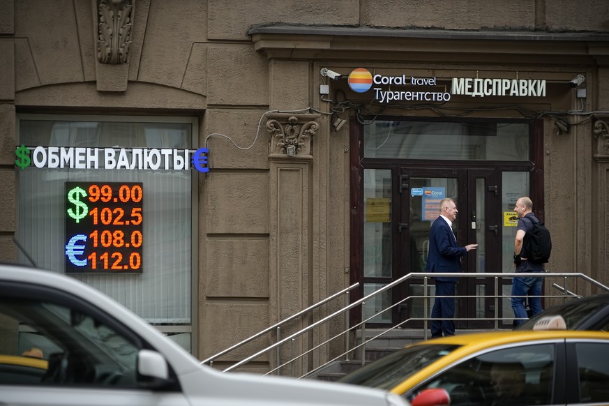 Deux hommes discutent à l'entrée d'un bureau de change à Moscou, lundi.