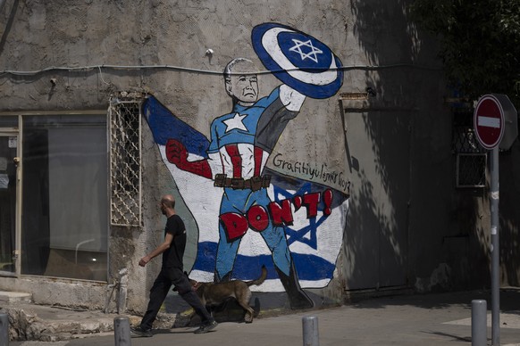 A man walks past a mural depicting the U.S. president Joe Biden as a superhero defending Israel on a street in Tel Aviv, Israel, Sunday, April 14, 2024. Israel on Sunday hailed its successful air defe ...