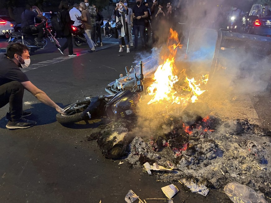 In this Monday, Sept. 19, 2022, photo taken by an individual not employed by the Associated Press and obtained by the AP outside Iran, a man pulls out a police motorcycle which is set on fire during a ...