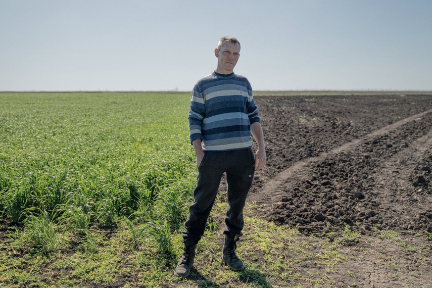 Igor Kniazev, 45 ans, agriculteur ukrainien, se tient devant son champ, divisé entre un champ encore contaminé par des mines terrestres et un champ décontaminé, dans le village de Dovhenke.