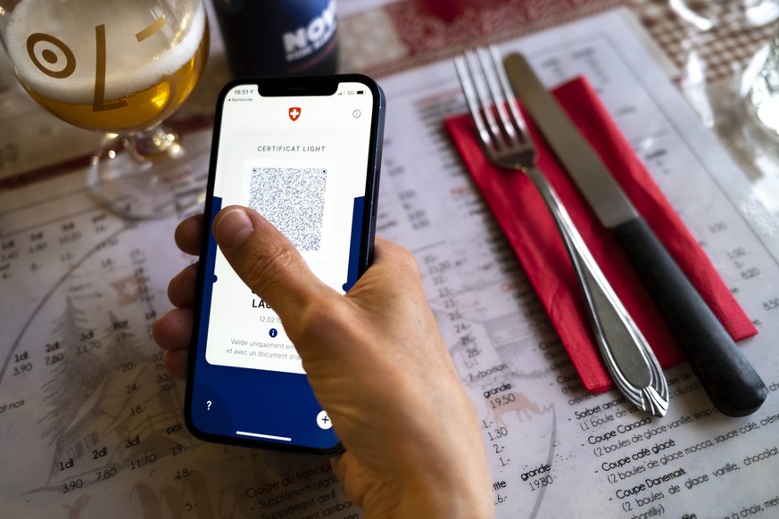 Une personne tient dans sa main un smartphone avec l&#039;application Certifact Covid suisse et un certificat light dans un restaurant ce vendredi 10 septembre 2021 a Rances dans le canton de Vaud. De ...