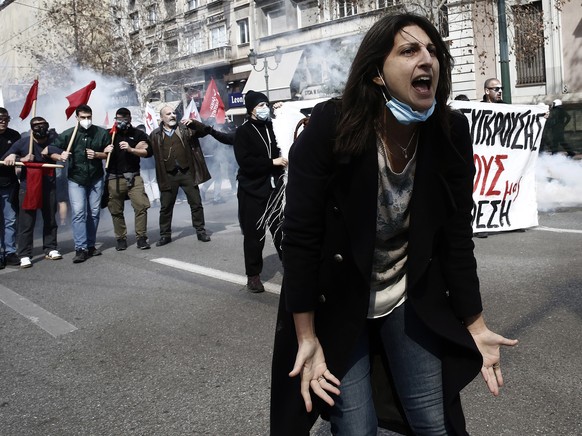 epaselect epa10504485 Protesters try to protect themselves from tear gas thrown by riot policemen during clashes after the end of a rally in honor of the 57 victims of Greece&#039;s deadliest train cr ...