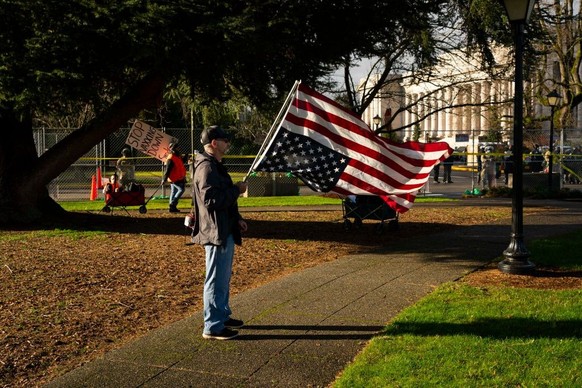 OLYMPIA, WA - JANUARY 10: A conservative demonstrator holds a U.S. flag upside down as an anti-vaccination demonstrator walks nearby at the Washington State Capitol campus on January 10, 2021 in Olymp ...