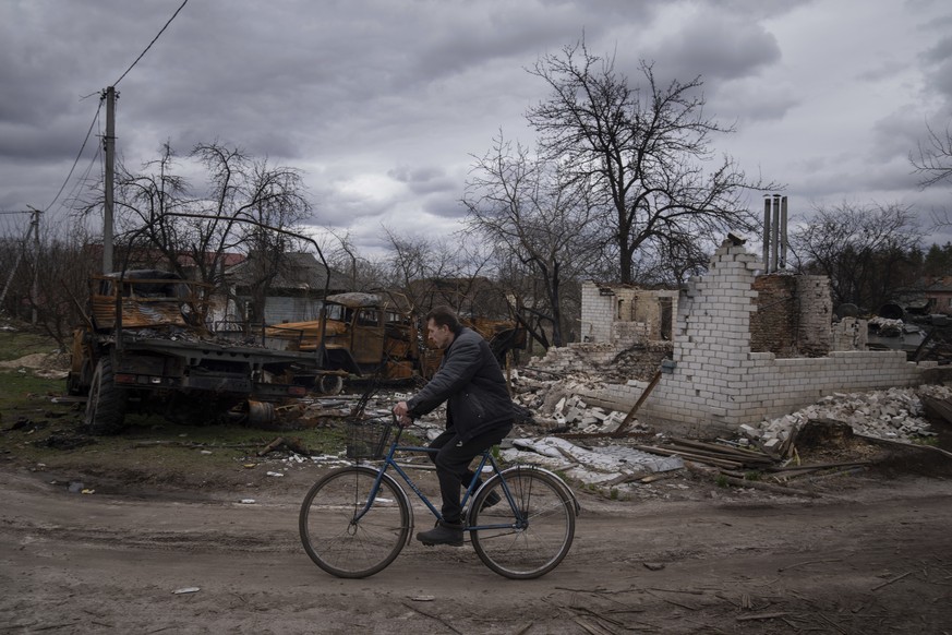 A man rides a bicycle past destroyed vehicles and an apartment building in Yahidne, near Chernihiv, Ukraine, Tuesday, April 12, 2022. Residents say more than 300 people were trapped for weeks by Russi ...