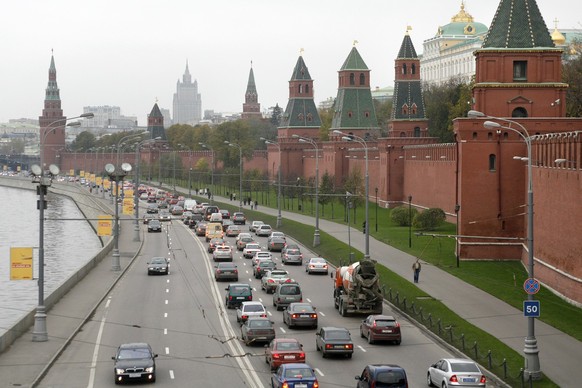 Des voitures circulent entre les murs et les tours du Kremlin, à droite, et la rivière Moskva, à gauche, sur la rue Kremlyovskaya à Moscou, en Russie, photographiée le 25 octobre 2006.