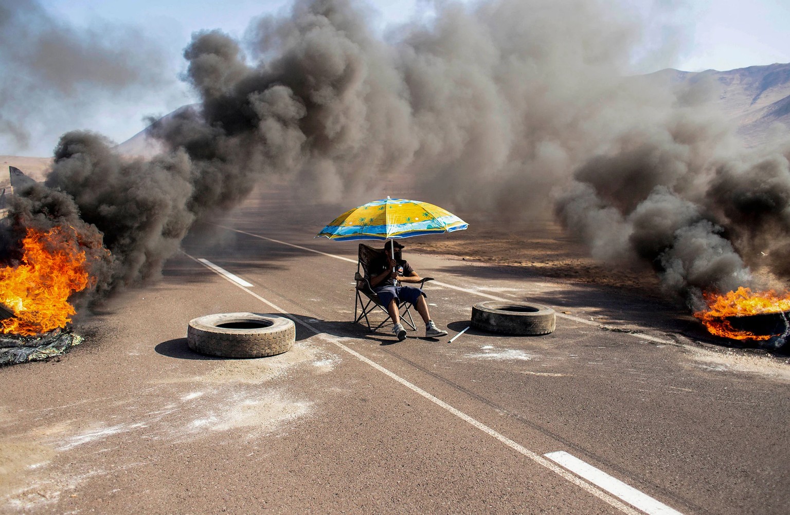 Un manifestant est assis sous un parasol, tout en bloquant une voie d'accès à Iquique, au Chili, lors d'une grève régionale menée par différentes organisations contre l'immigration clandestine, le 31  ...