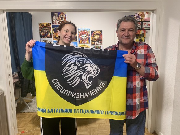 Serhii et sa fille Sofiia tenant le drapeau de son unité de combat. En arrière-fond, des tableaux peints par Larysa.