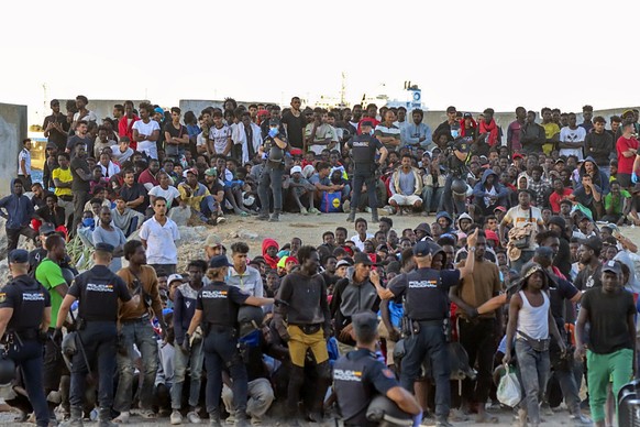 epa13150615 Police officers direct migrants at El Trampolin beach in Ceuta, Spain, 04 August 2026. According to Spanish officials, around 2,500 migrants remain in Ceuta following last week's mass ...