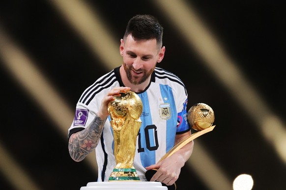 epa10373265 Lionel Messi of Argentina touches the World Cup trophy as he passes it after winning the golden ball award during the awards ceremony after the FIFA World Cup 2022 Final between Argentina  ...