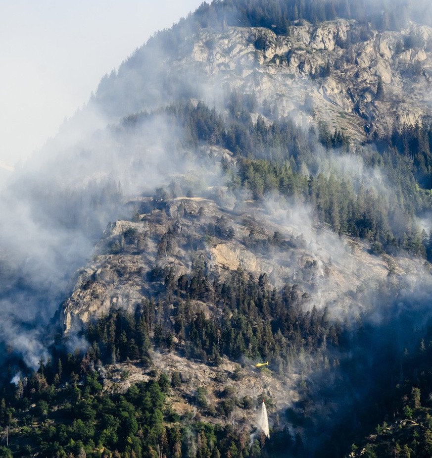 Un helicoptere verse de l'eau sur la fumee qui s'echappe de la foret en feu au dessus des communes de Bitsch et Ried-Moerel le mardi 18 juillet 2023 depuis Termen. Les h