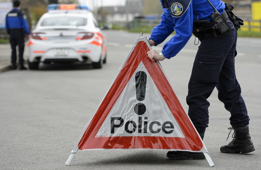 [Editor&#039;s note: photo mise-en-scene] A police officer from the cantonal police of Vaud installs a police warning triangle, in the foreground, while another officer stands next to a police car, in ...