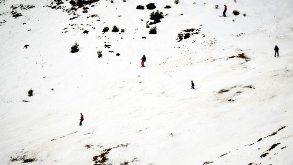 Skiers speed down a ski slope between Roc d&#039;Orsay and Bretaye with a lack of snow and the grass appearing, at 2000 meters above sea level, in the alpine resort of Villars-sur-Ollon, Switzerland,  ...