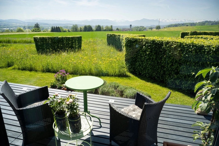 Un jardin où haies taillées, pelouse et végétation jouent sur les formes géométriques, avec vue sur la campagne.