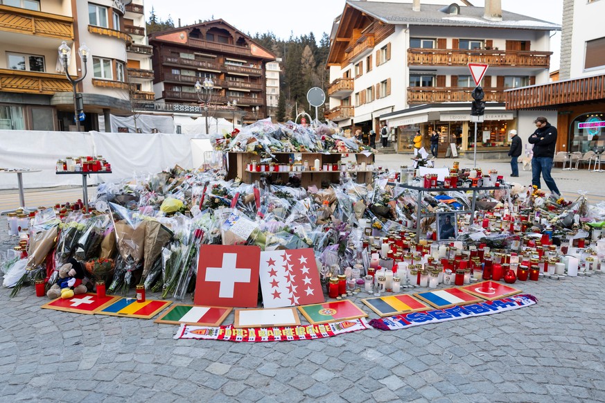 Plaques bearing flags representing Switzerland, Romania, Italy, Portugal, Belgium, France, and Turkey are placed along with flowers and candles to honor the victims of the fire at the "Le Constel ...