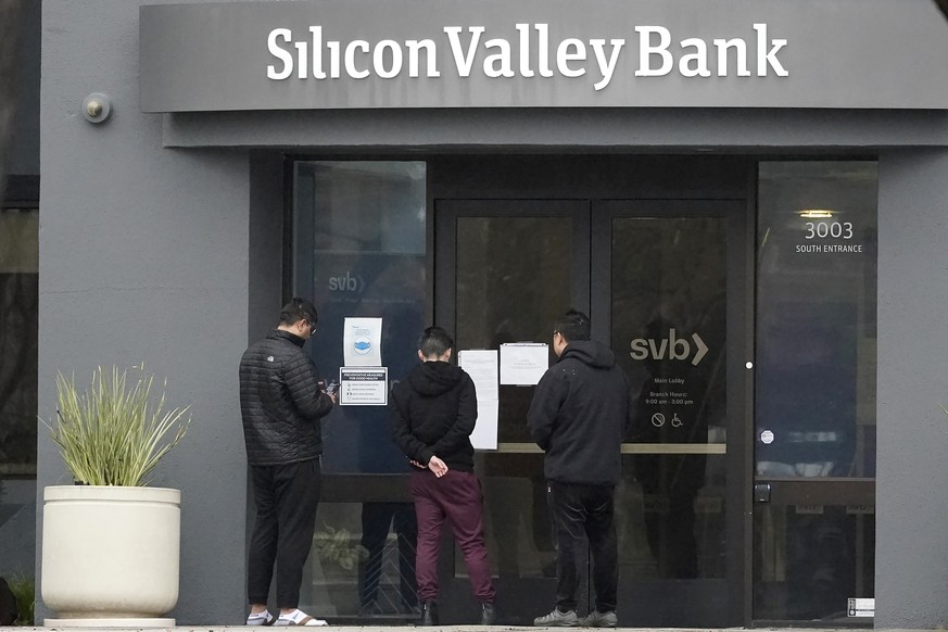 FILE -People look at signs posted outside of an entrance to Silicon Valley Bank in Santa Clara, Calif., Friday, March 10, 2023. While Wall Street struggles to contain the banking crisis after the swif ...