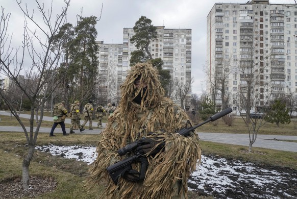 Ukrainian Territorial Defence Forces members walk past the city park as a camouflaged soldier stands in foreground, in the outskirts of Kyiv, Ukraine, Wednesday, March 9, 2022. Authorities announced a ...