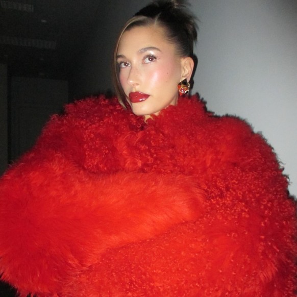 Hailey Bieber, son gros manteau, ses grosses boucles d'oreilles, son gros rouge à lèvres. Un look très «mob wife».