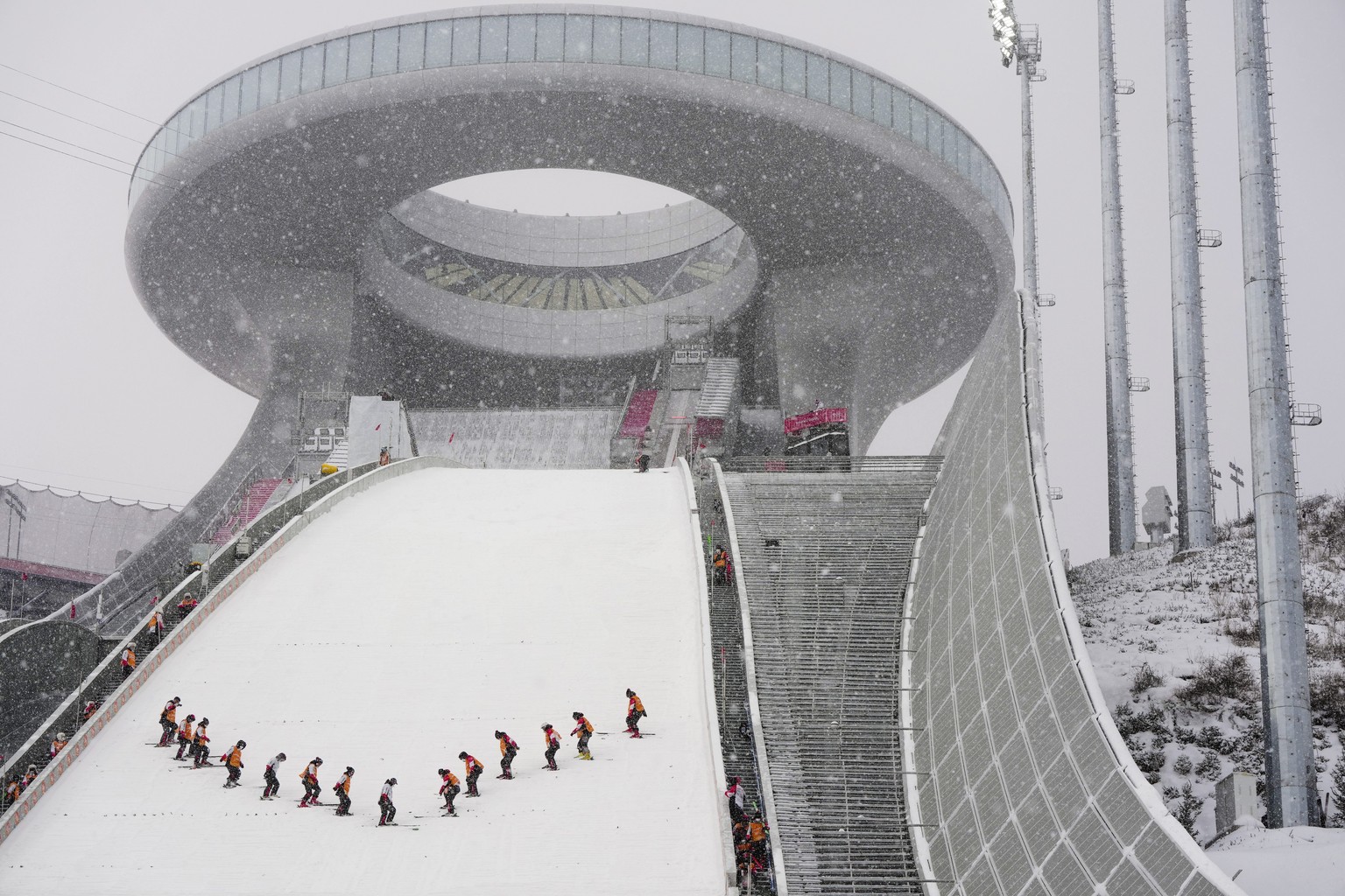 People work on the hill as snow falls at Zhangjiakou National Ski Jumping Centre at the 2022 Winter Olympics, Sunday, Feb. 13, 2022, in Zhangjiakou, China. (AP Photo/Matthias Schrader)