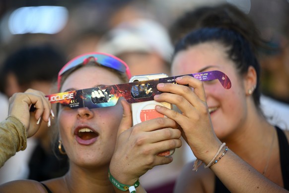 epa13164552 Festival-goers take pictures with a mobile phone and a pair of protective eclipse viewing glasses while observing the Sun during a partial solar eclipse at the 30th Venoge Festival in Pent ...