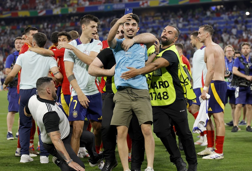 epa11469429 A security guard (L bottom) slides into Spanish player Alvaro Morata as he tried to join his colleagues removing a pitch invader (C) taking a selfie in front of Spanish players celebrating ...