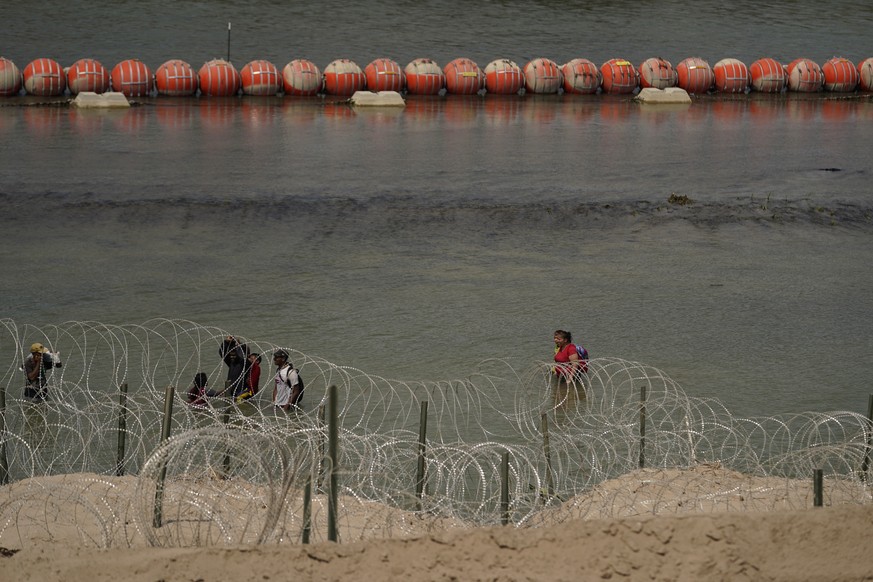 Migrants from Columbia walk along Concertina wire and a floating buoy barrier after crossing the Rio Grande from Mexico into the U.S., Monday, Aug. 21, 2023, in Eagle Pass, Texas. (AP Photo/Eric Gay)