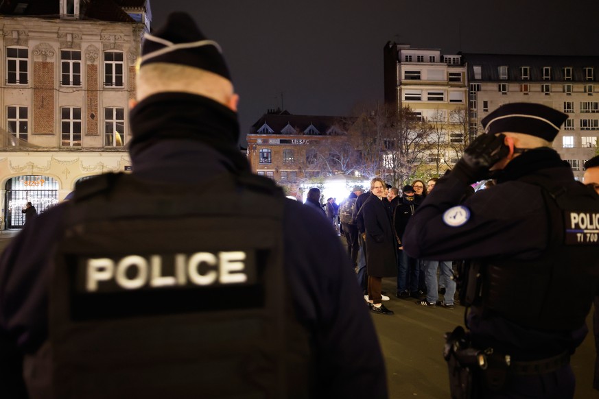 Police officers stand near people gathered to pay a tribute to far-right student, Quentin Deranque, 23, who died in Lyon from a street beating during clashes between far-left and far-right militants,  ...