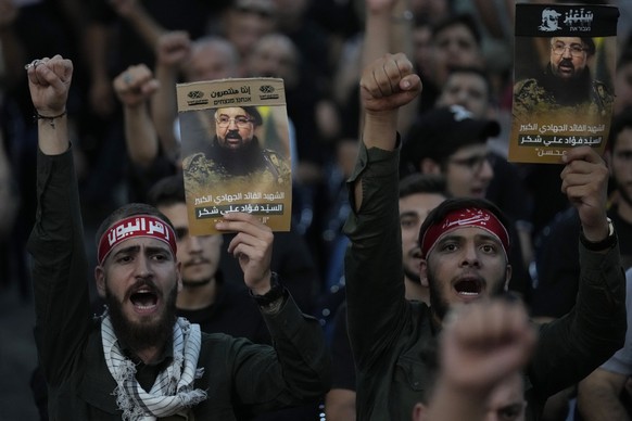 FILE -Hezbollah supporters shout slogans and hold up portraits that show the top commander Fouad Shukur, who was killed by an Israeli airstrike on Tuesday, July 30, during his funeral procession in a  ...