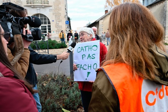 A woman holds a placard reading &quot;catholic, not fascist&quot; as she answers a journalist&#039;s question during a protest in front of the Saint-Jean-Baptiste church, where takes place a religious ...