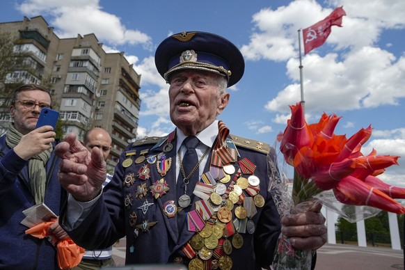 Vladimir Kapitonovin, 98 ans, vétéran de la Seconde Guerre mondiale et ancien pilote militaire, fait un geste en parlant à un groupe de journalistes étrangers avec un drapeau rouge, une réplique de la ...