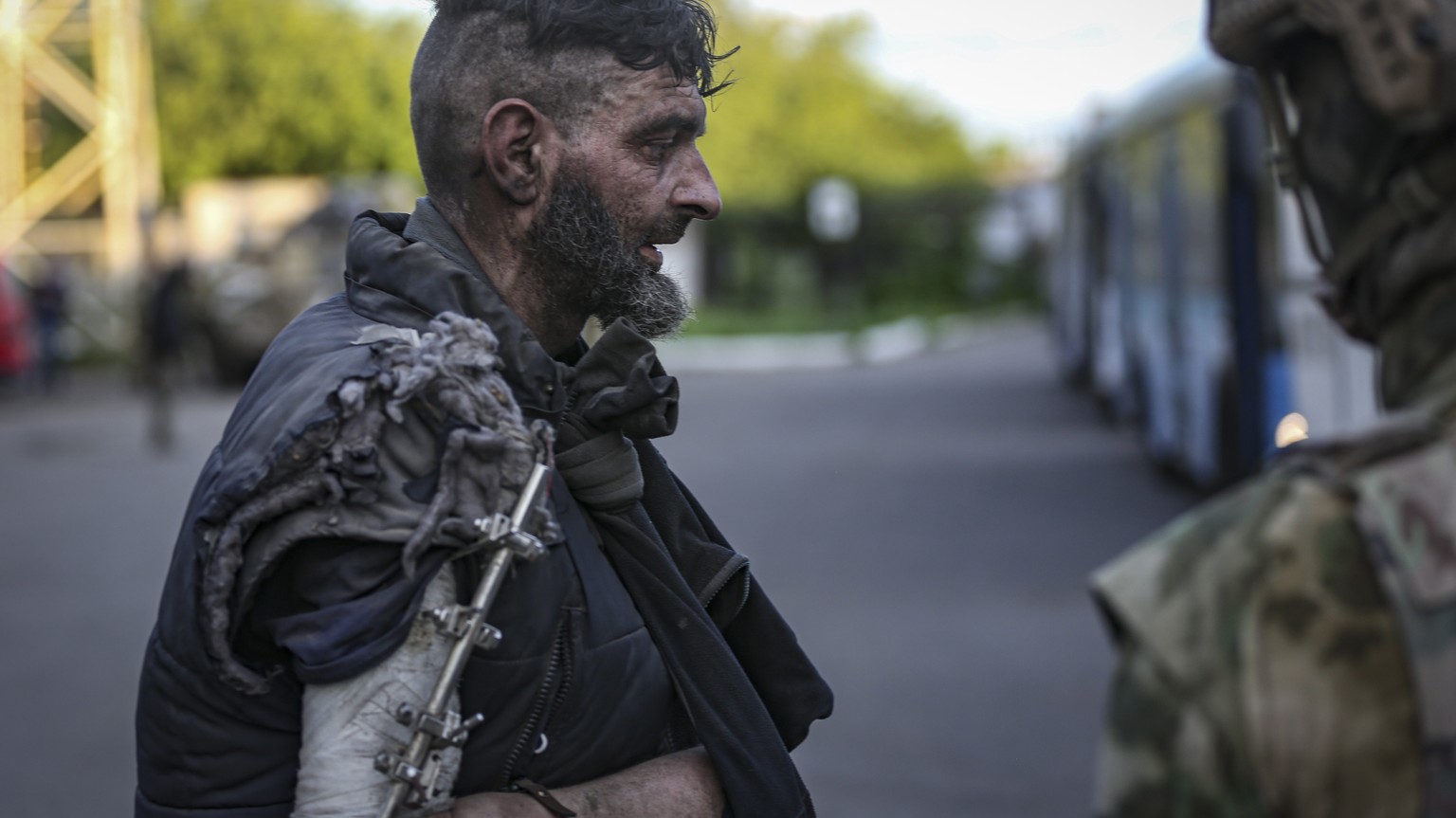 epa09953883 Self-proclaimed DPR militia (R) watches an Ukrainian serviceman boarding a bus as he is being evacuated from the besieged Azovstal steel plant in Mariupol, Ukraine, 17 May 2022. A total of ...