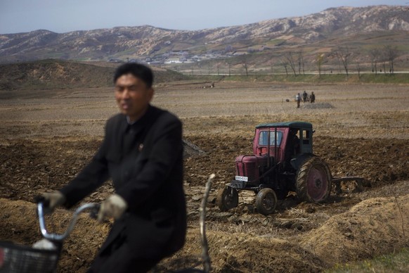 In this April 24, 2013 photo, a North Korean man passes by on a bicycle as a farmer in a tractor works in his field southeast of Kaesong, North Korea near the demilitarized zone that separates the two ...