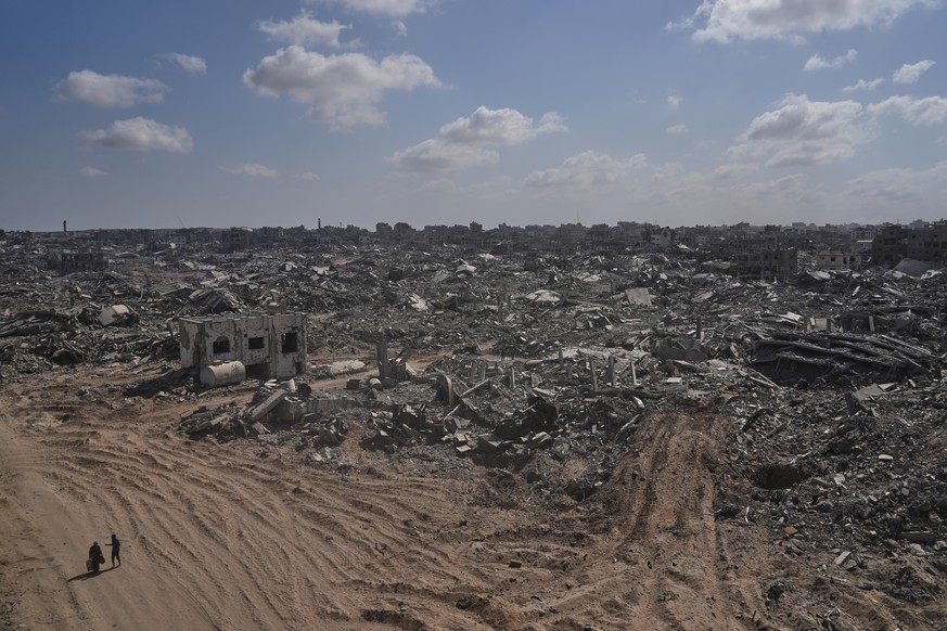 Two displaced Palestinians walk past destroyed buildings in the heavily damaged Sheikh Radwan neighborhood in Gaza City, Saturday, Oct. 11, 2025, after Israel and Hamas agreed to a pause in their war  ...