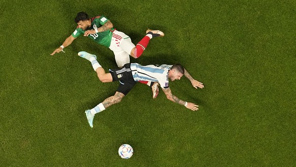 Mexico's Alexis Vega, top, falls to the ground in a clash with Argentina's Rodrigo De Paul during the World Cup group C soccer match between Argentina and Mexico, at the Lusail Stadium in Lusail, Qata ...