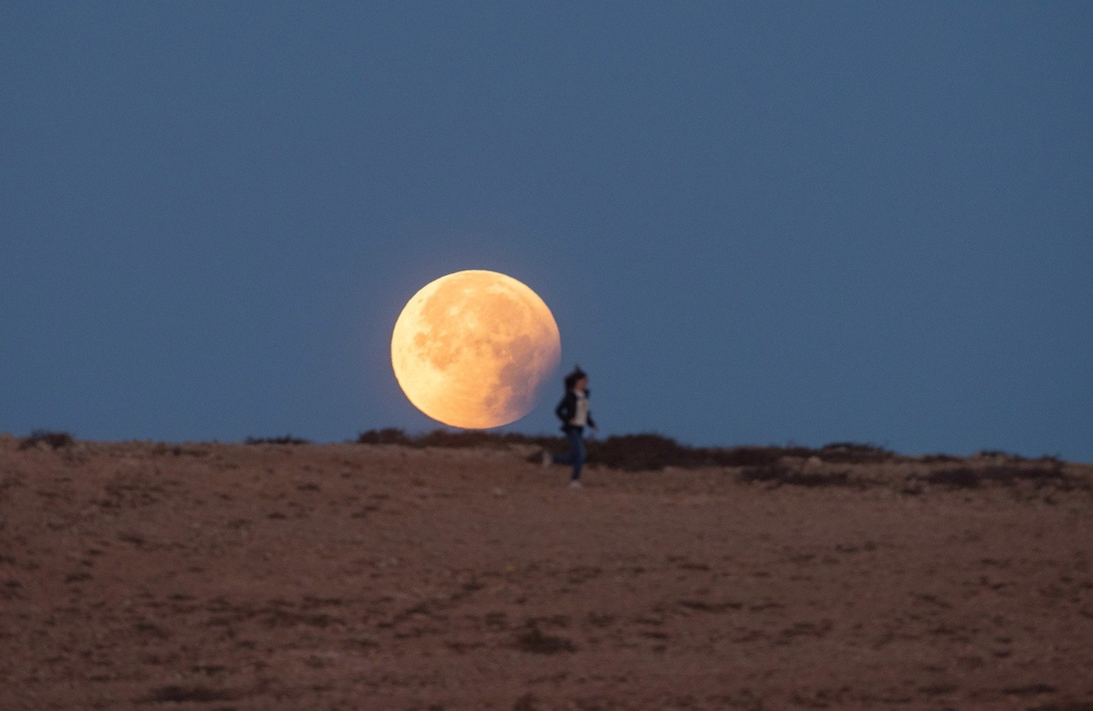 Une femme court devant la Lune pendant une éclipse dans le village de Tindaya, sur l'île de Fuerteventura, dans le sud-ouest de l'Espagne, tôt le 16 mai 2022.