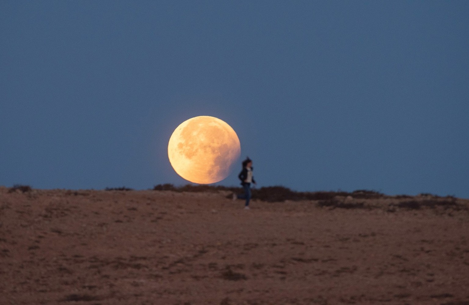 Une femme court devant la Lune pendant une éclipse dans le village de Tindaya, sur l&#039;île de Fuerteventura, dans le sud-ouest de l&#039;Espagne, tôt le 16 mai 2022.