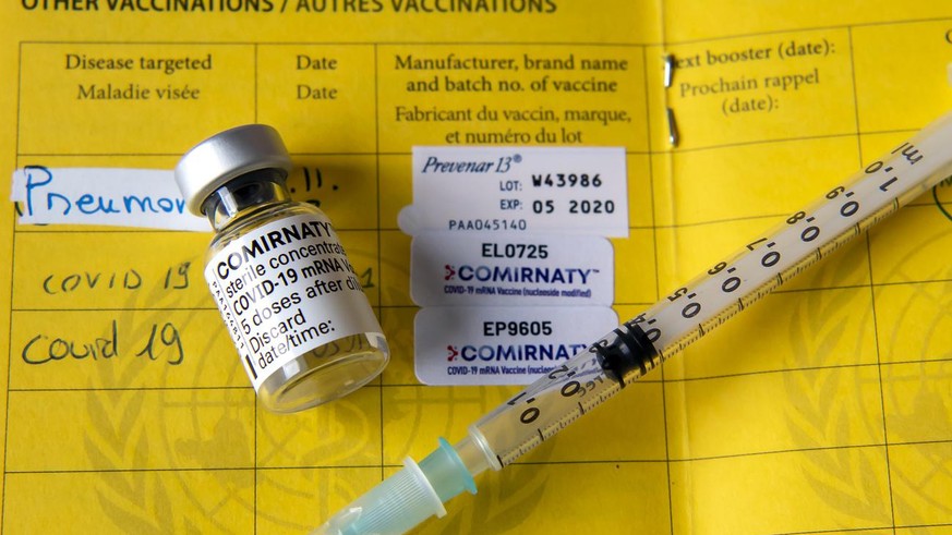 Une fiole du vaccin Pfizer-BioNTech et une seringue sont photographiees sur un carnet de l&#039;OMS de certificat international de vaccination ou de prophylaxie, faudra-t-il un jour un passeport vacci ...