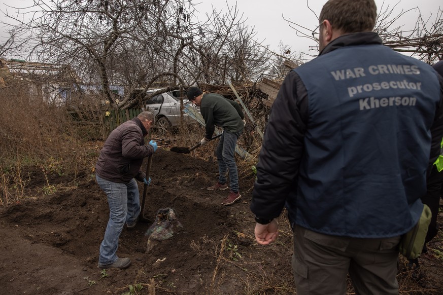 epa10335451 Residents help police officials, forensic experts, and war crime prosecutors to exhume the bodies of six civilians from a mass grave at a yard in the village of Pravdyne, outside Kherson,  ...
