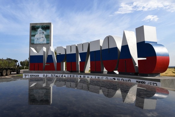 A Russian military truck passes a road sign reading &quot;Mariupol&quot; and painted in the colours of the Russian national tricolor flag in the Russian-controlled Azov Sea port city of Mariupol in so ...