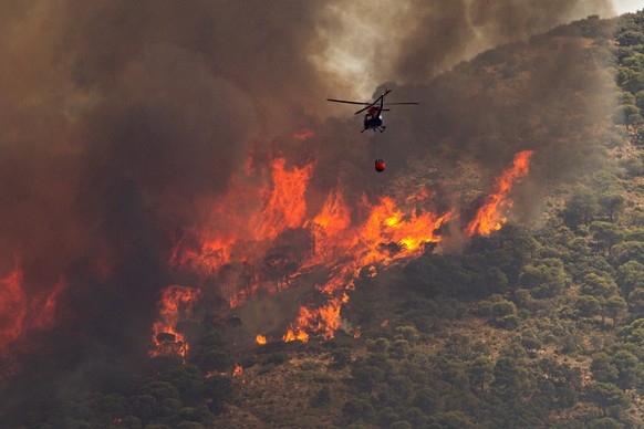 epa10072820 A helicopter pours water into the flames of a forest fire in Mijas, Malaga, southern Spain, 15 July 2022. Regional authorities activated the first level of the Emergency Plan for Forest Fi ...