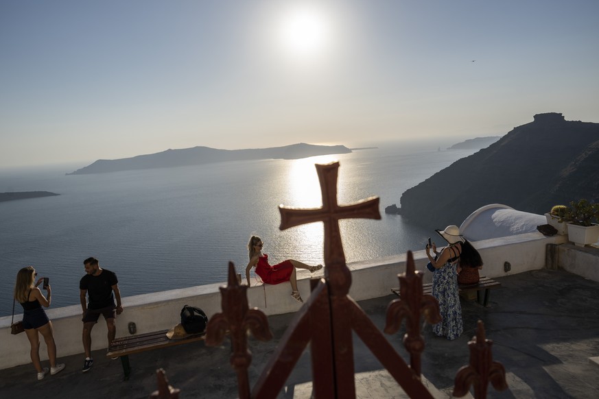A woman poses for a photograph outside the wrought-iron enclosure of the Dormition of the Virgin Mary Catholic Church on the Greek island of Santorini on Wednesday, June 15, 2022. The Monastery of St. ...